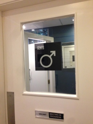 Men's room door featuring window and signage from former use as office space