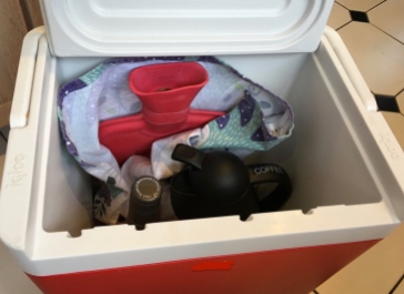 Cooler stocked with hot water bottle, coffee and wine for outdoor guests in cold weather