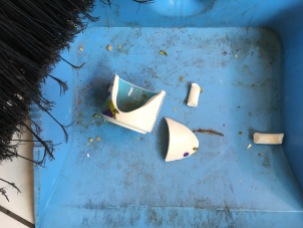 shards of decorated ceramic in dustpan next to broom