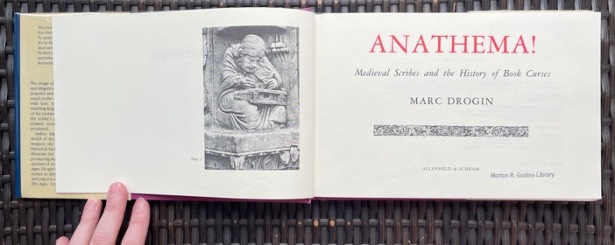 Open copy of unusually wide but short hardcover book Anathema! Medieval scribes and the history of book curses